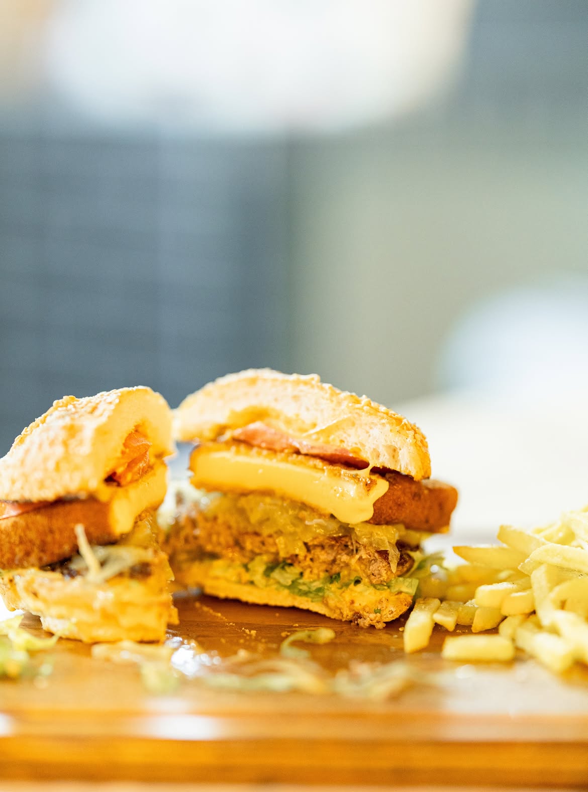 Burger cut in half on a wooden board with a side of chips
