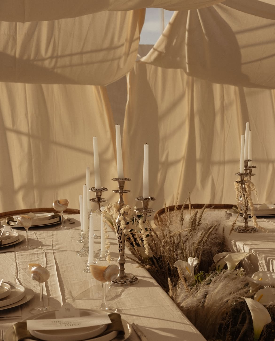 Candlelit long table beneath flowing linen drapes at golden hour