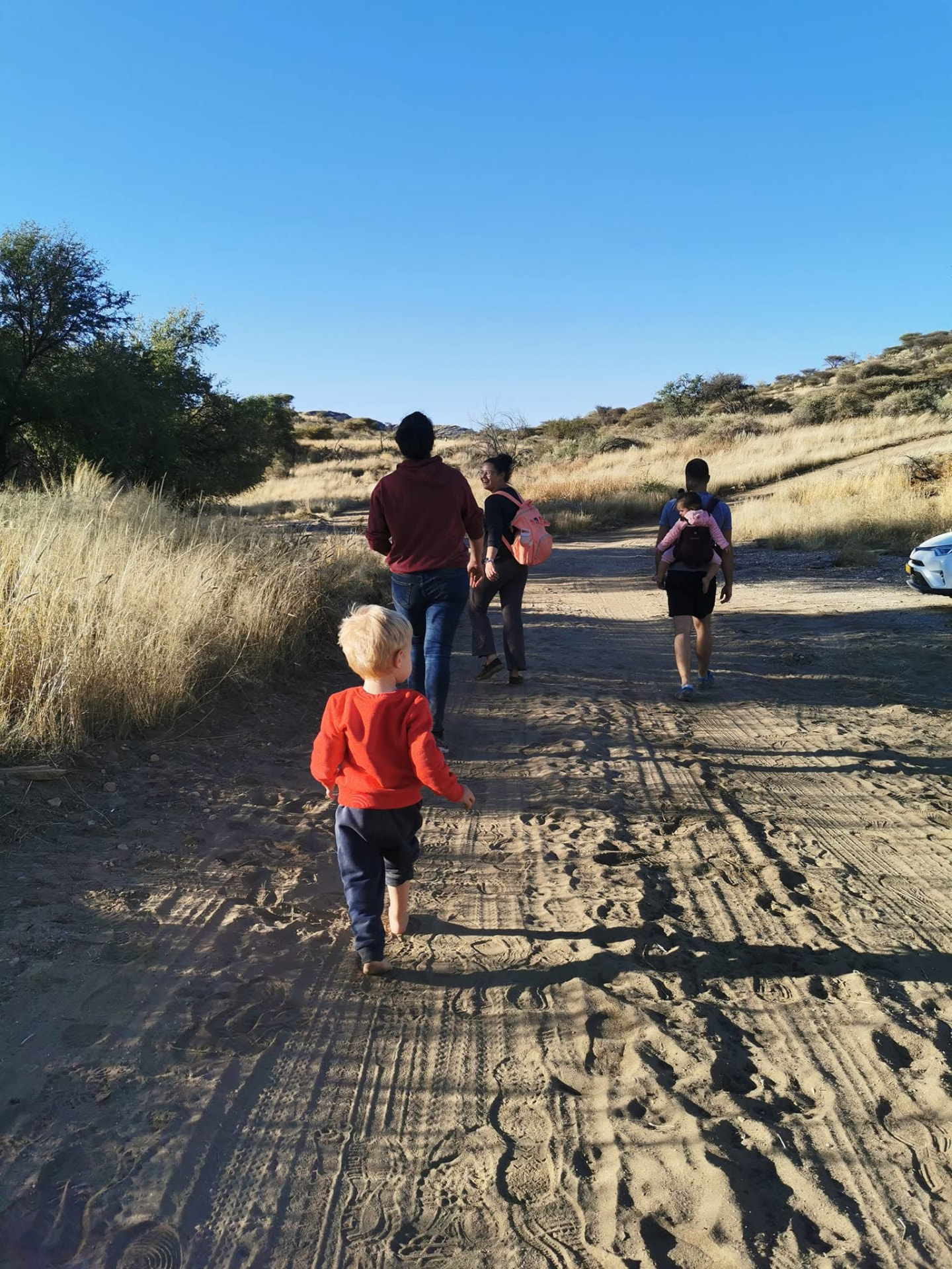Family with a toddler walking barefoot along the sandy trail