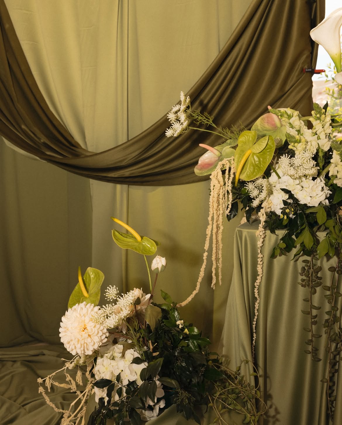 Floral installation of anthuriums and dahlias against olive silk drapery