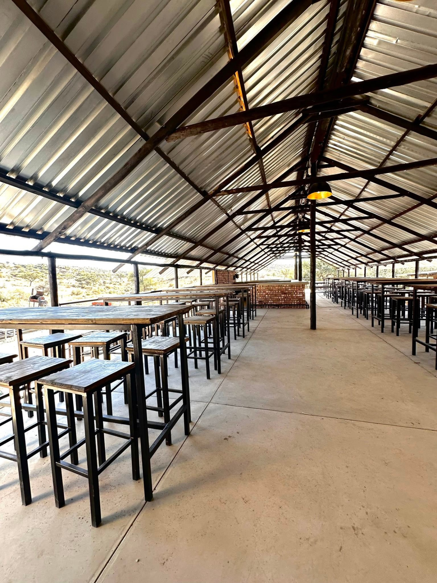 Long undercover hall with rows of high wooden tables and stools looking out over the bush