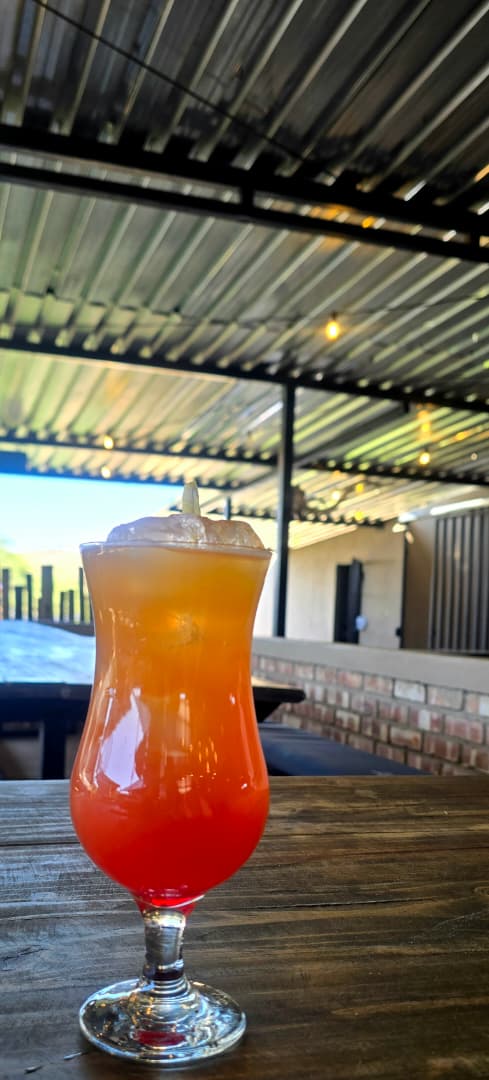 Tall iced drink layered red, orange and yellow on a wooden table under the covered patio