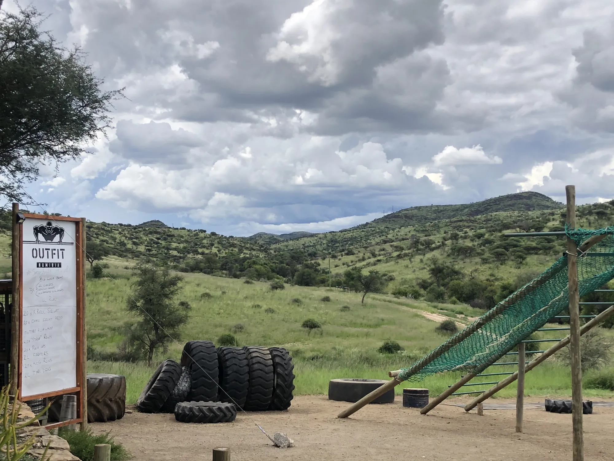 Tractor tyres and a green cargo net on the Outfit Namibia obstacle course with the Windhoek hills behind