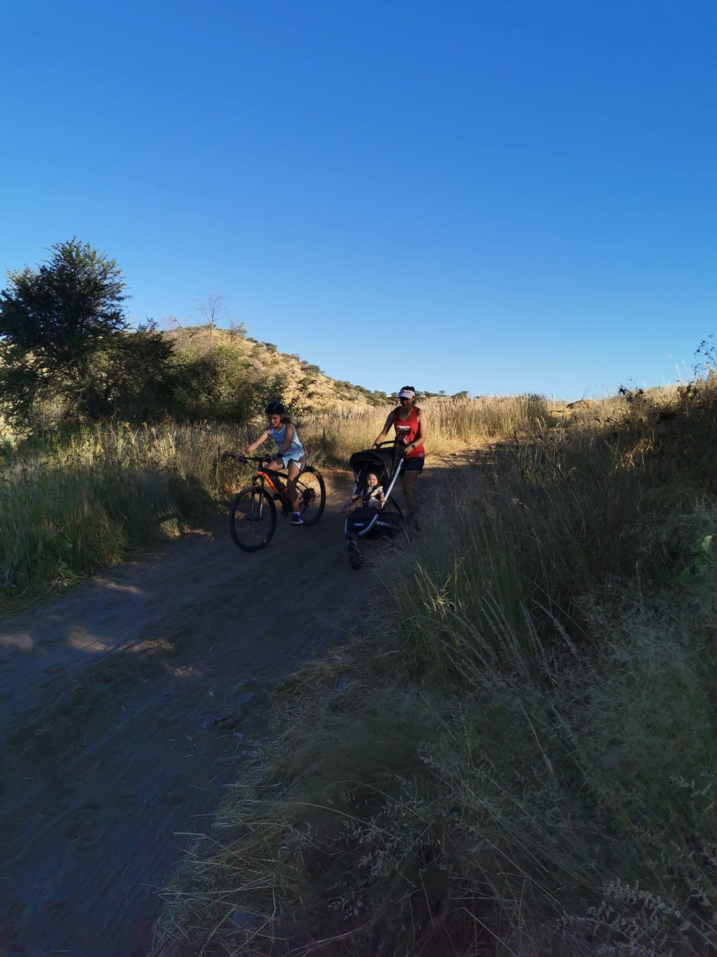 Young cyclist and a mom pushing a pram along the grassy trail