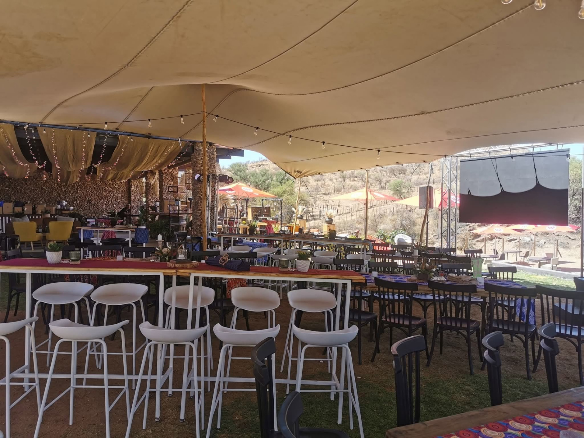 Bar counter with high stools and long tables under a stretch tent facing the stage