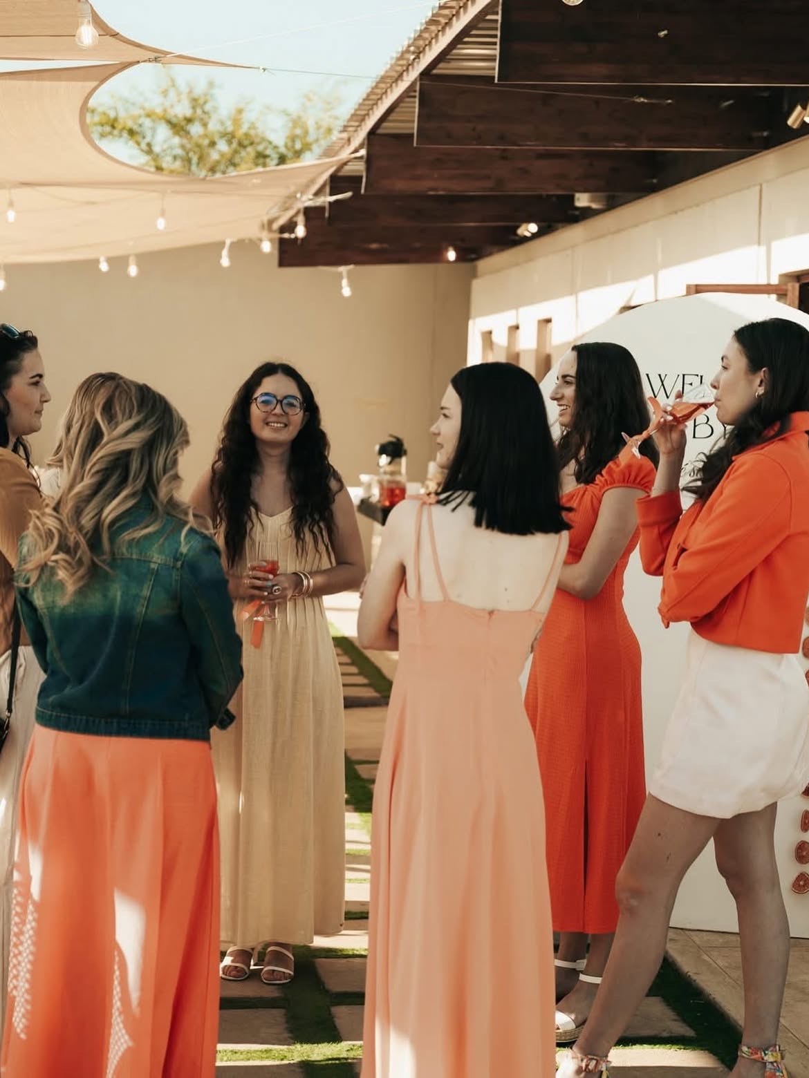 Guests with drinks under shade sails and festoon lights at a kitchen tea