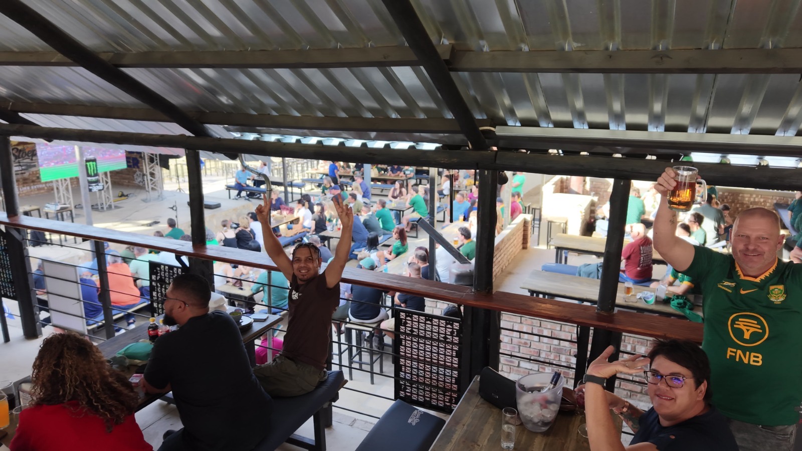 Guests raising a beer and cheering during a match on the big screen