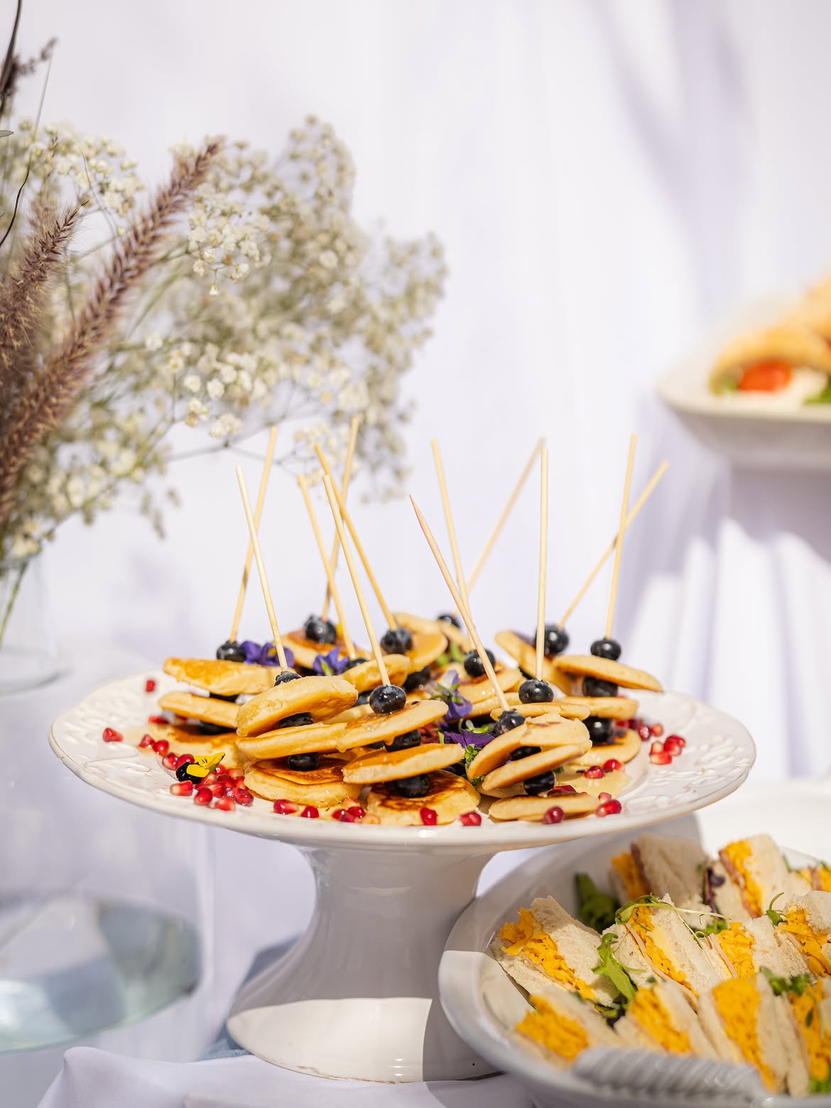 Blueberry-topped baked cheesecake on a stand with mini quiches behind