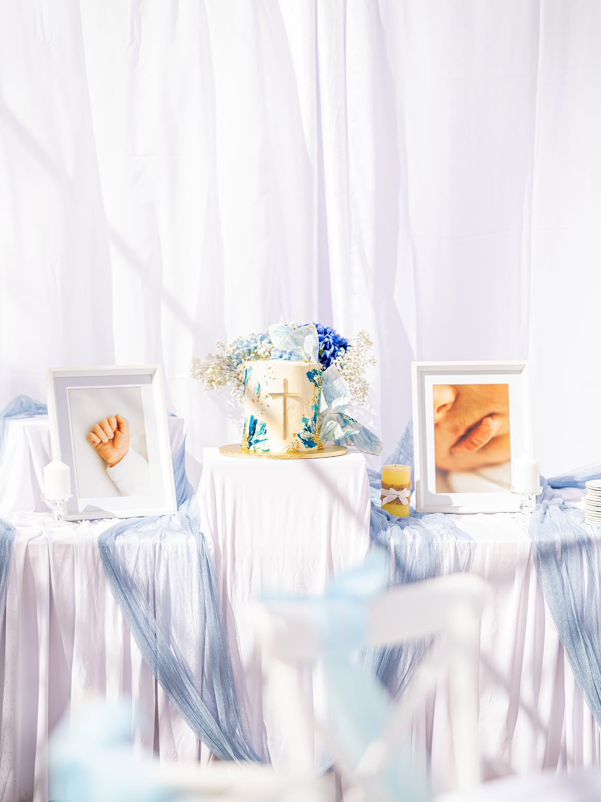 Christening cake table with framed photographs, candles and blue tulle draping