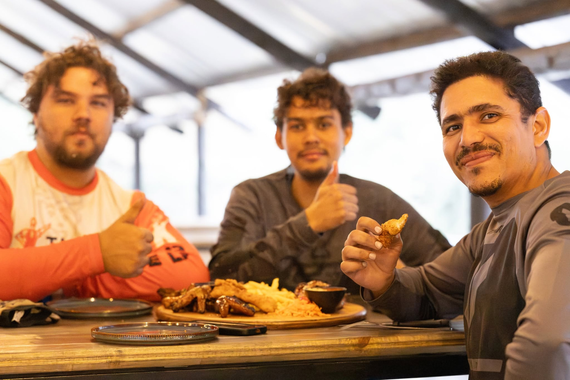 Three friends giving a thumbs up over a shared platter of wings and chips