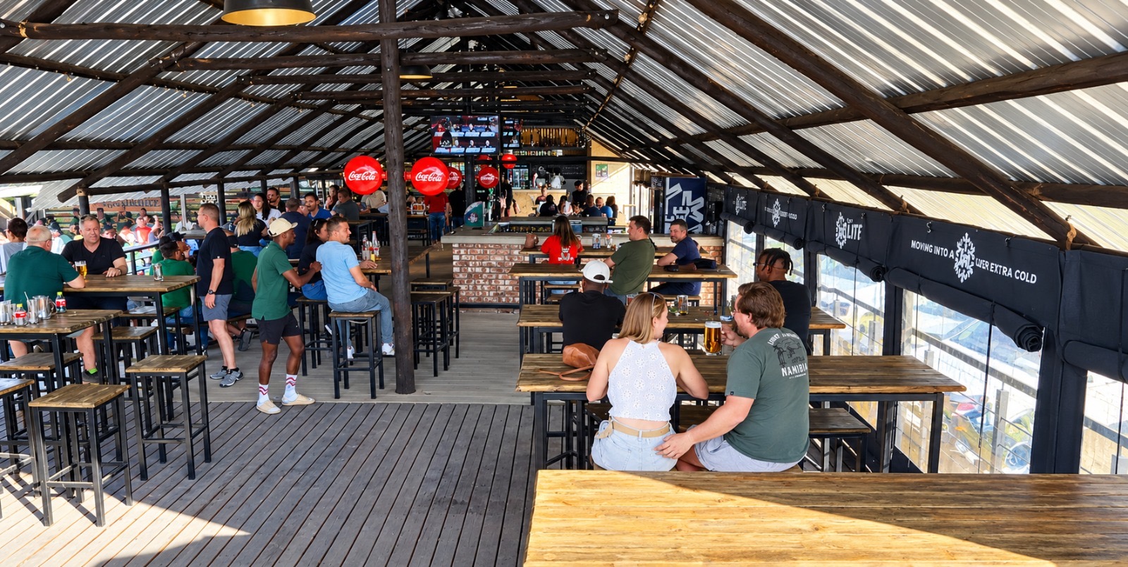 Busy Oppie Stoep bar hall with long tables, brick bar counter and big screens