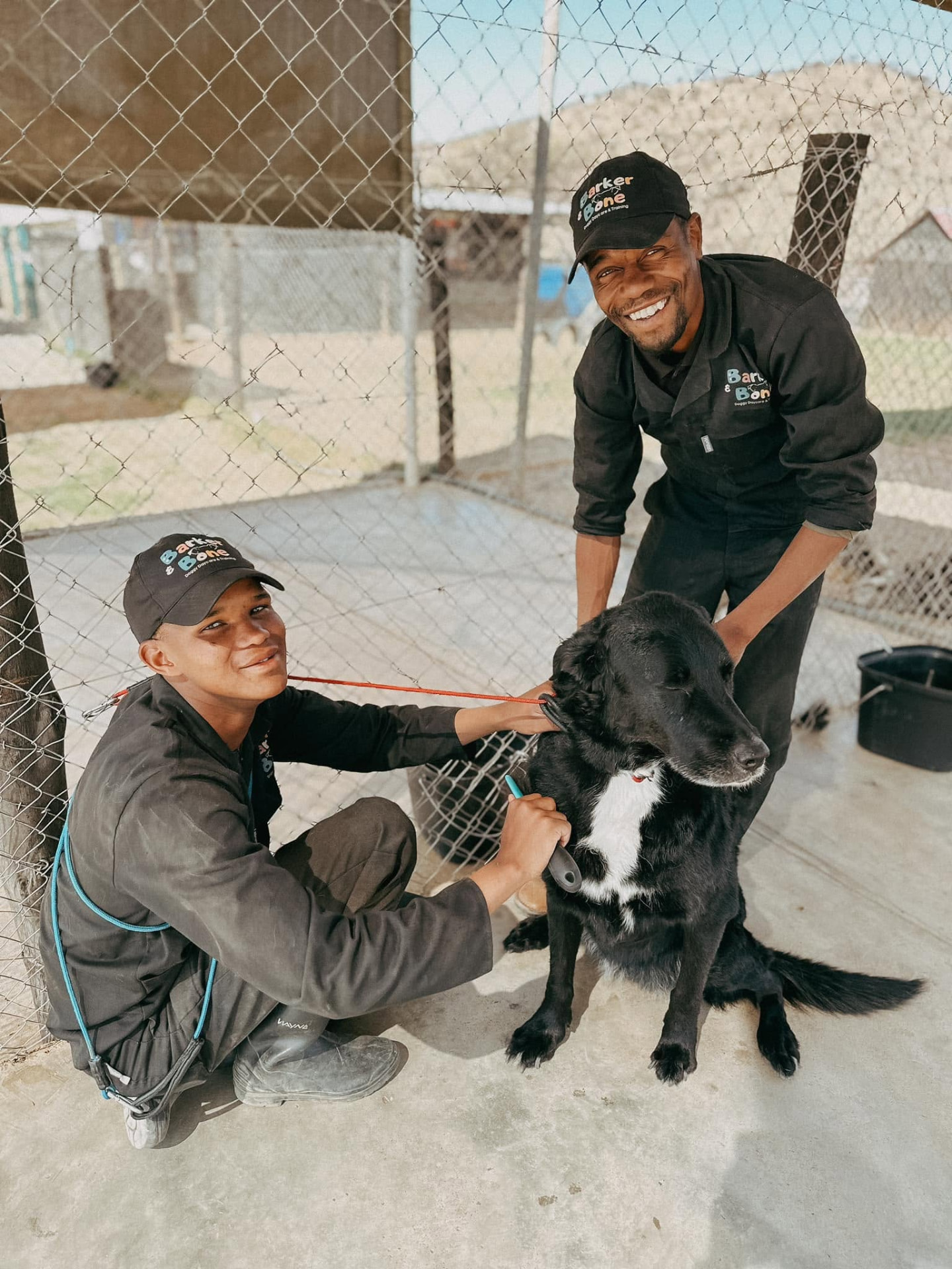 Two Barker & Bone team members grooming a black dog