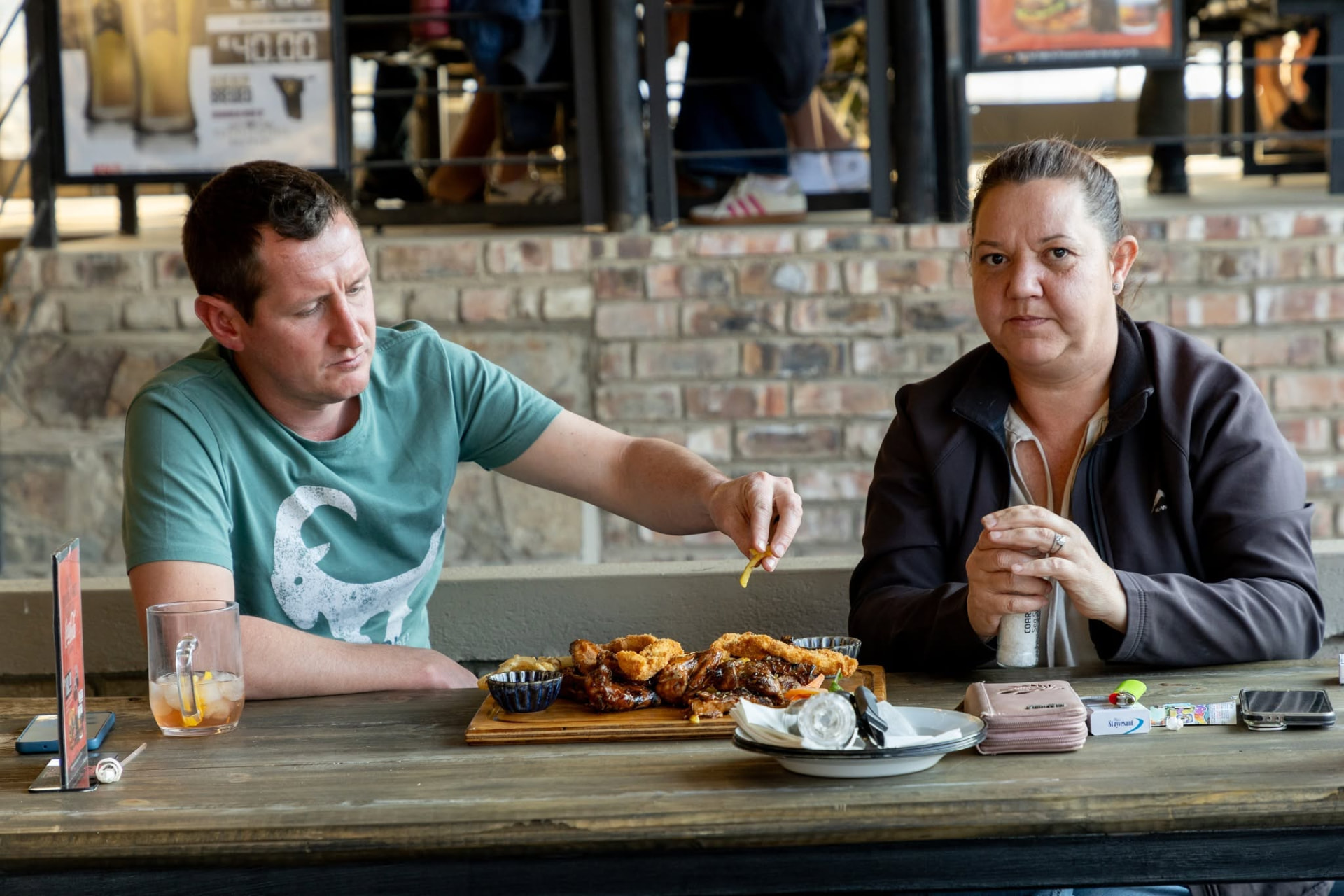 A couple sharing a grill platter at a wooden table on the stoep