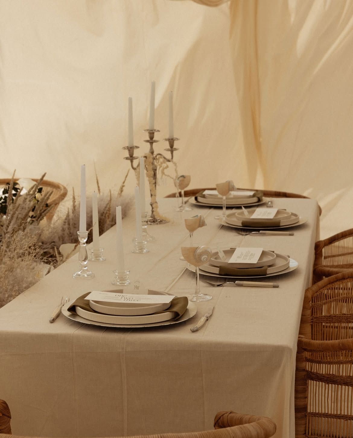 Linen-set table with taper candles, rattan chairs and dried grasses