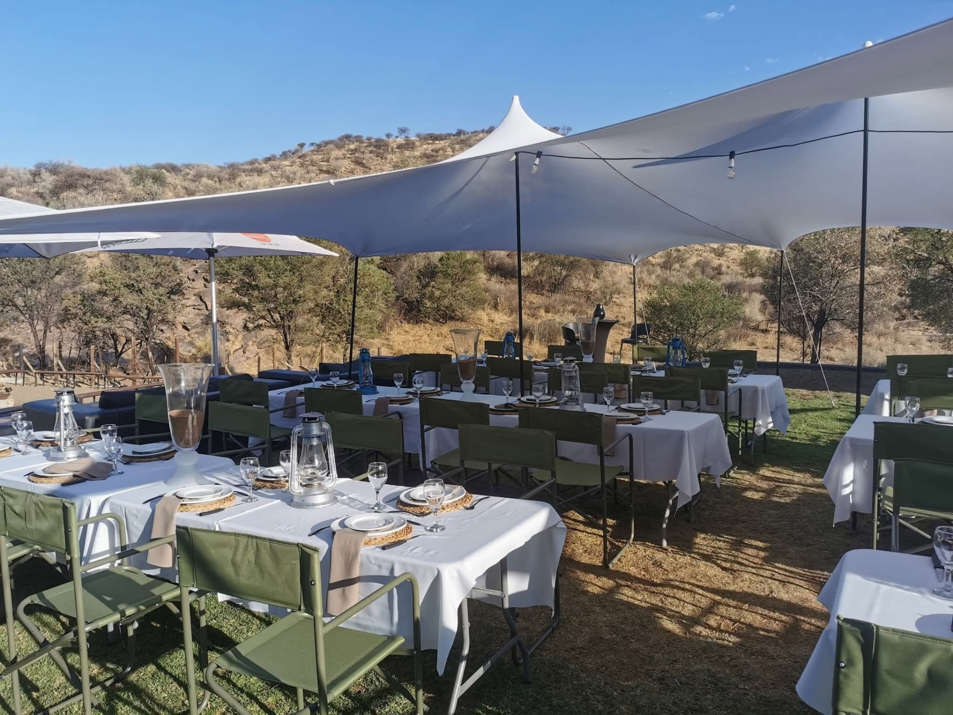 White stretch tents over laid tables on the lawn with the hillside behind