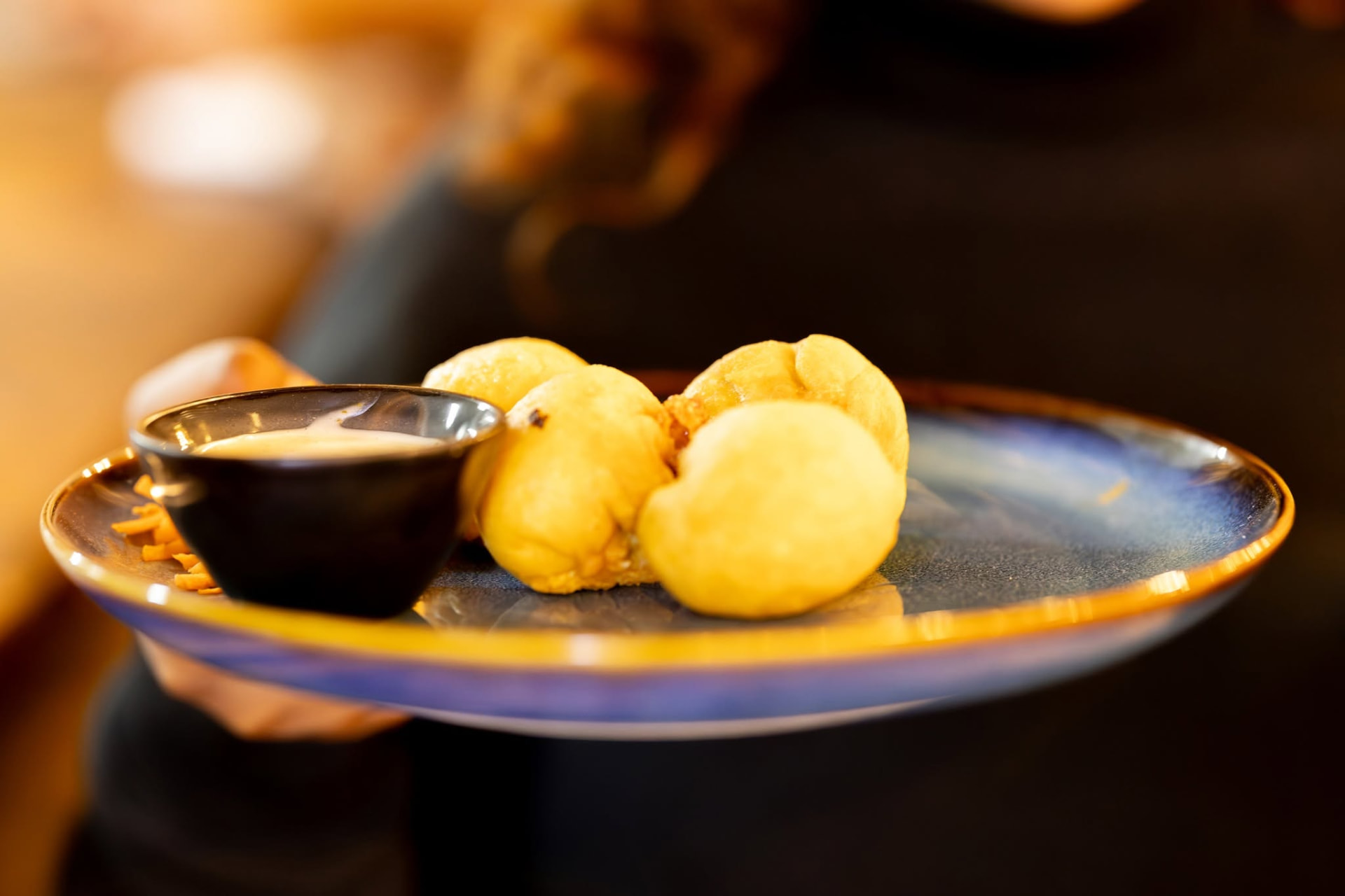 Golden fried dough balls served with a dipping sauce on a blue plate
