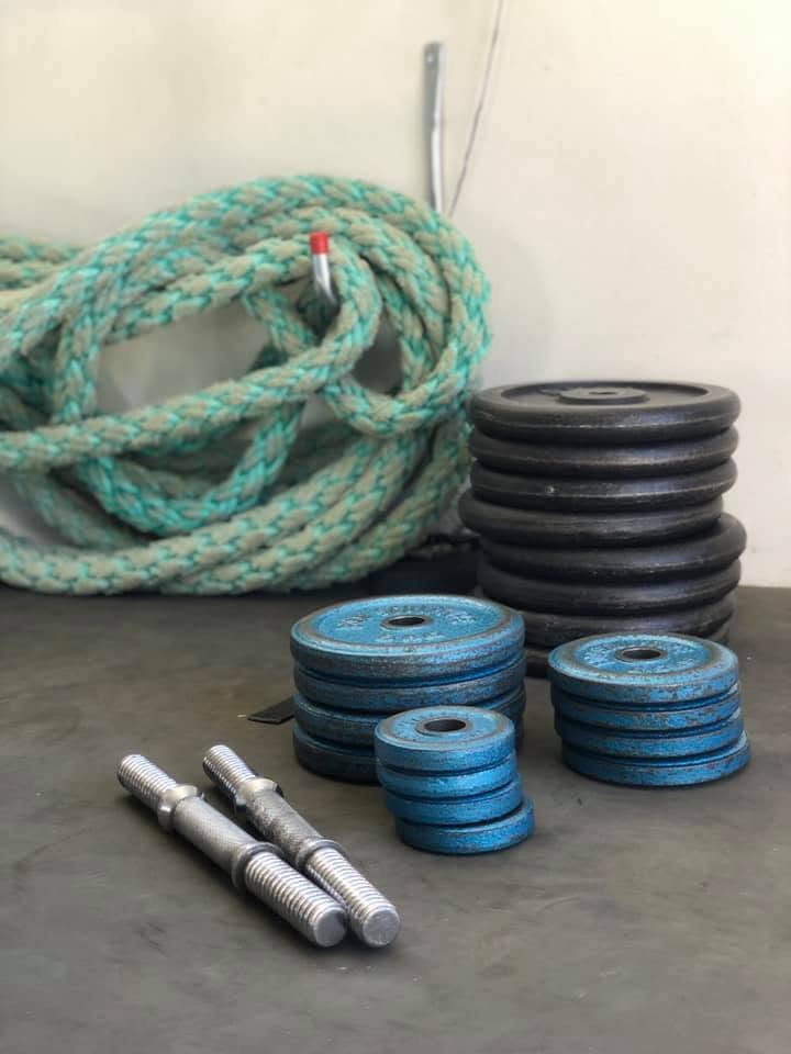 Climbing rope coiled beside stacked weight plates and dumbbell handles