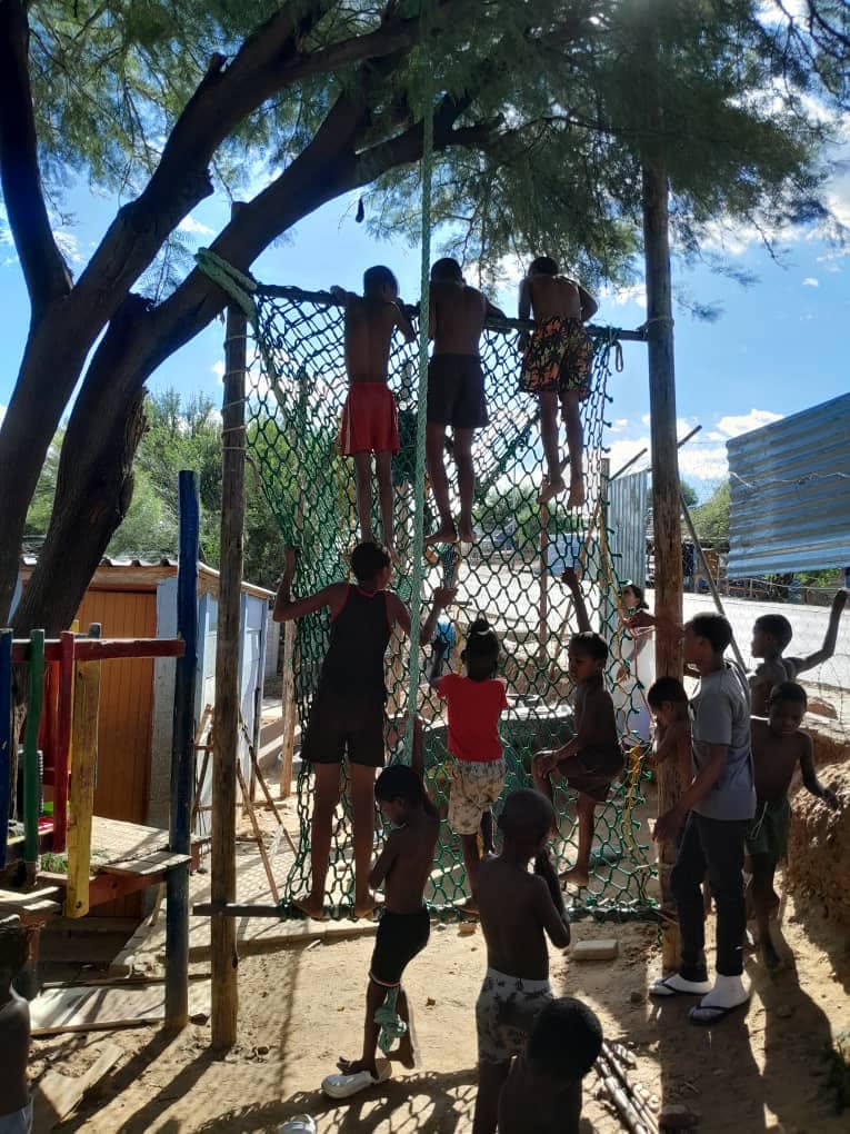 Children climbing a cargo net on a newly built community obstacle frame