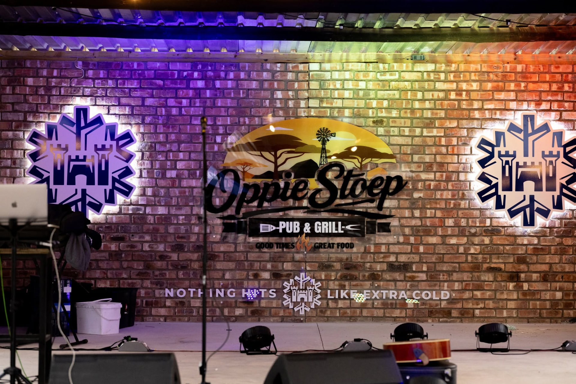 Oppie Stoep Pub & Grill sign lit up on the brick stage wall