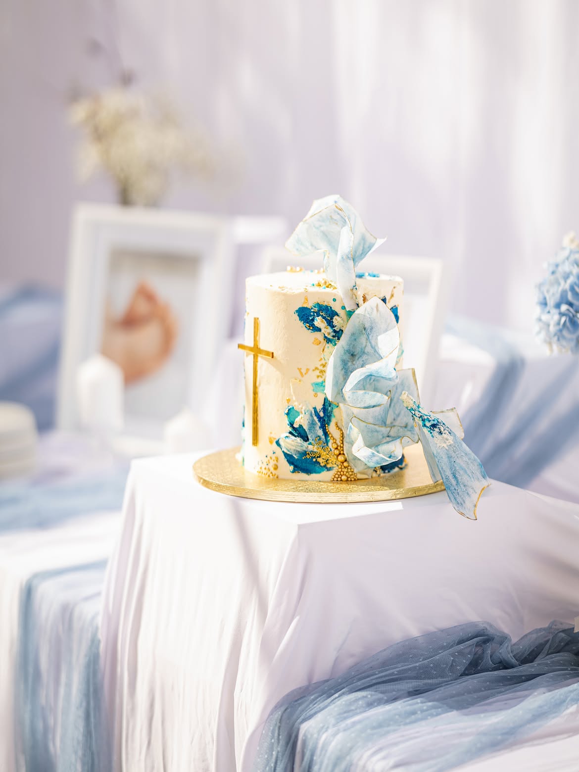 White and gold christening cake with blue sugar sails and a gold cross
