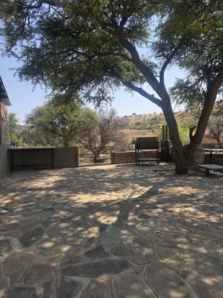 Shaded stone patio under a large tree with braai facilities