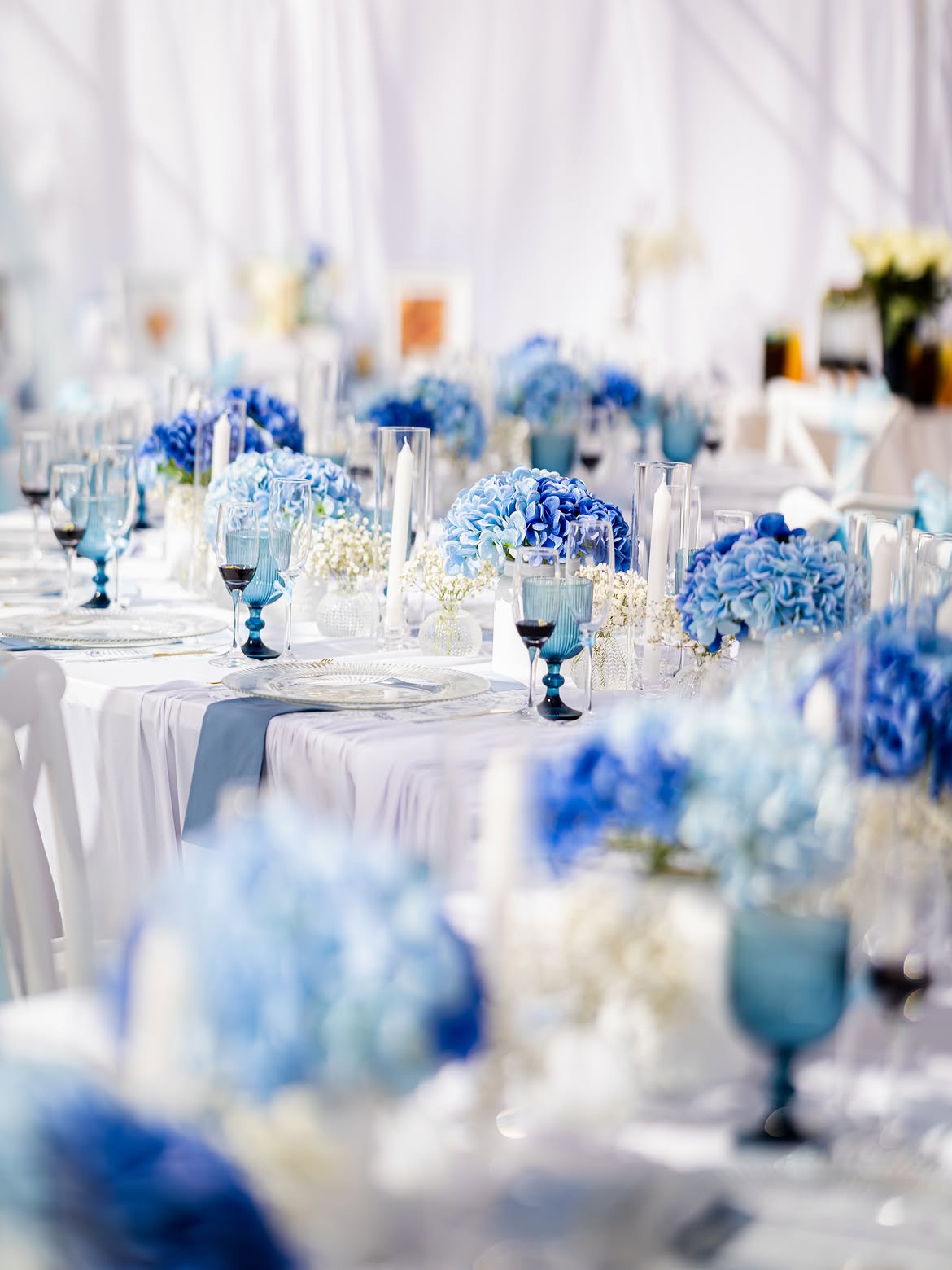 Long table lined with blue hydrangeas, taper candles and blue glassware