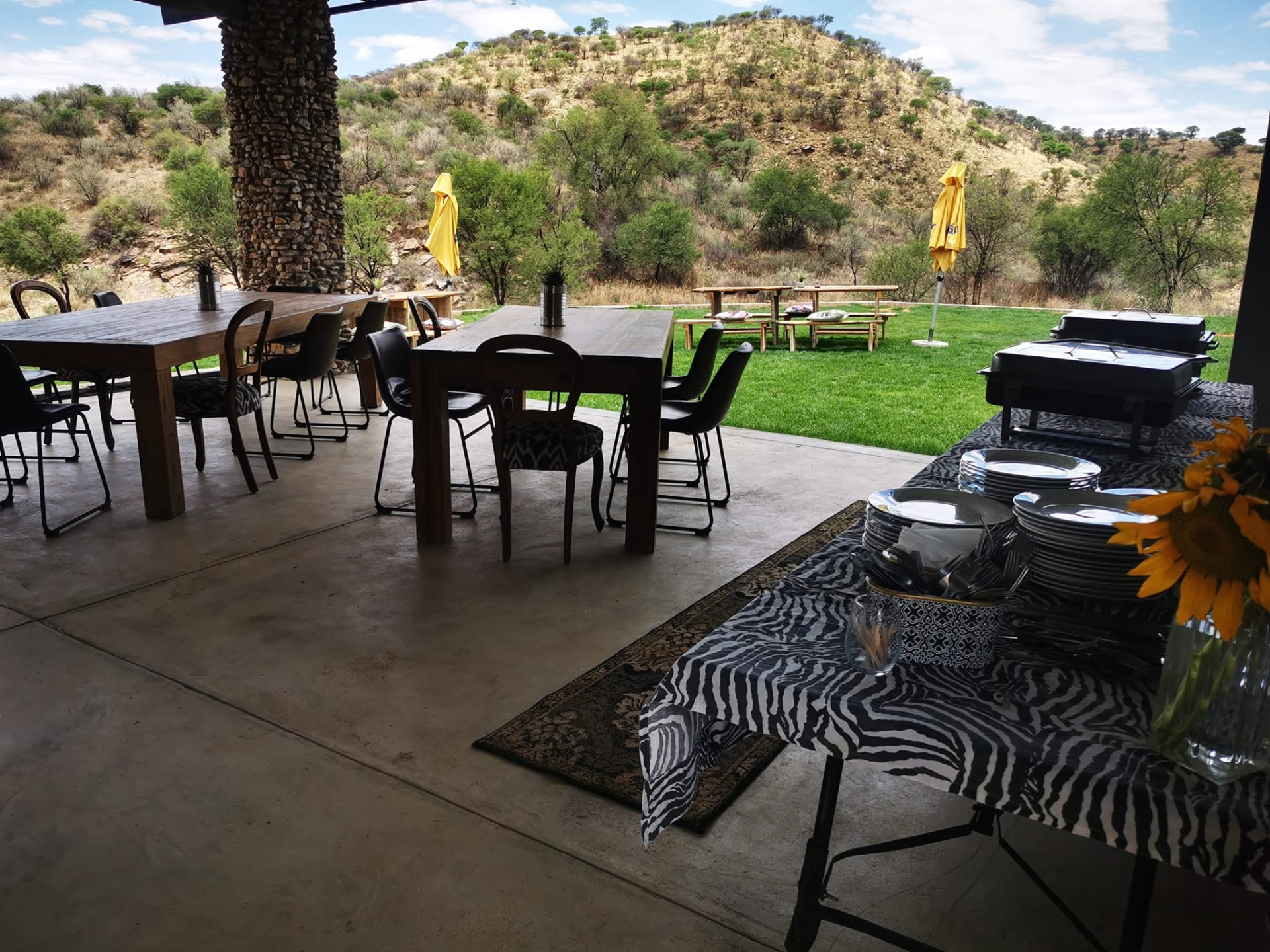 Covered stone patio with wooden tables looking out over the lawn and hillside