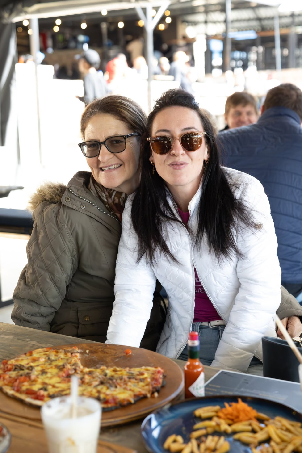 Two guests smiling over a wood-fired pizza at a long table