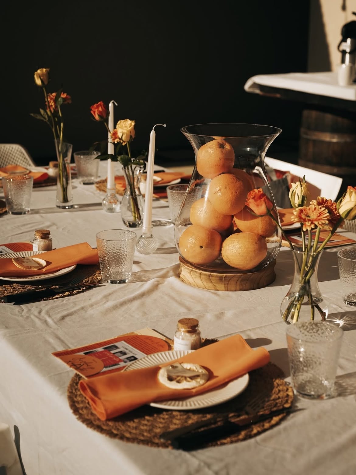 Table set with orange napkins, citrus centrepiece and taper candles in late light