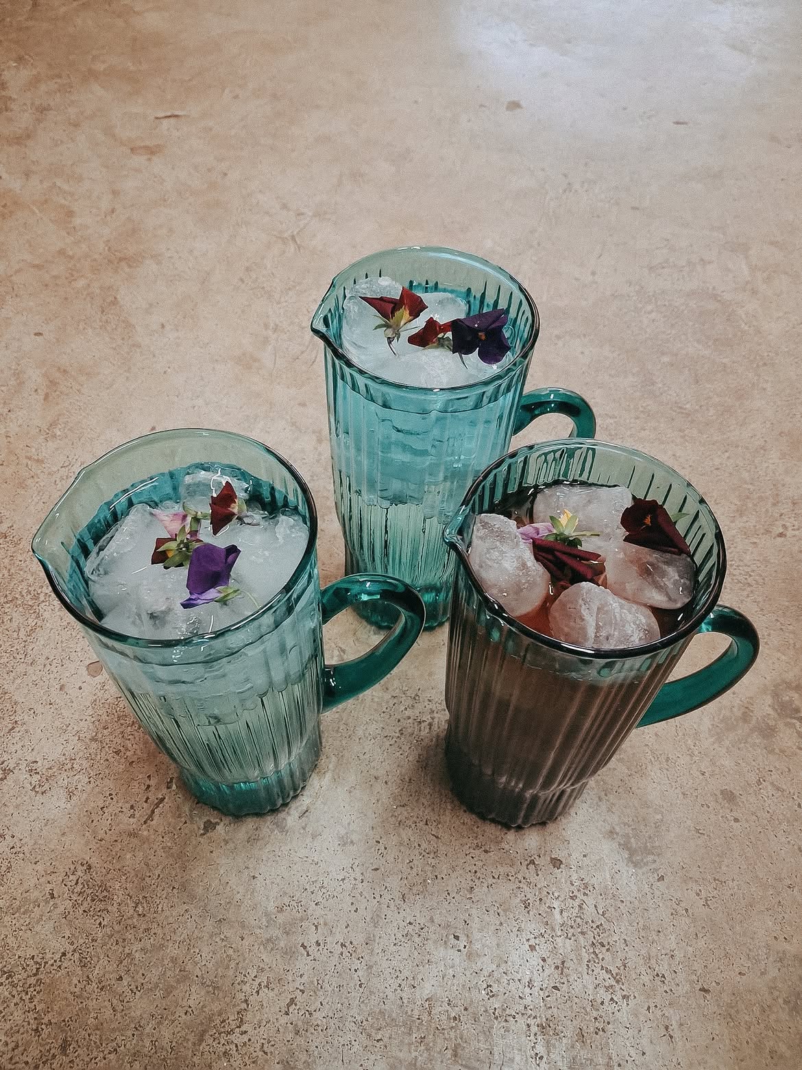 Green glass jugs of iced drinks finished with edible flowers