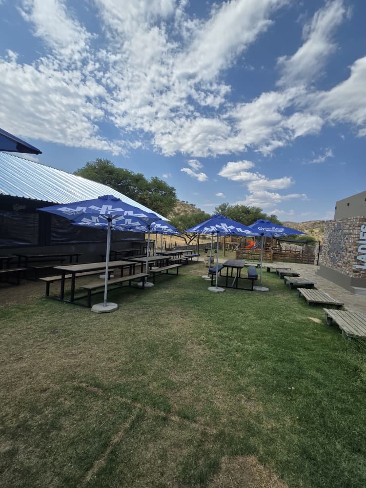 Beer garden with blue branded umbrellas on the lawn at Oppie Stoep