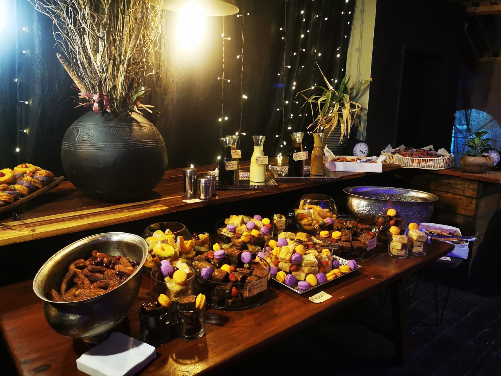 Dessert table with churros, macarons and brownies under fairy lights