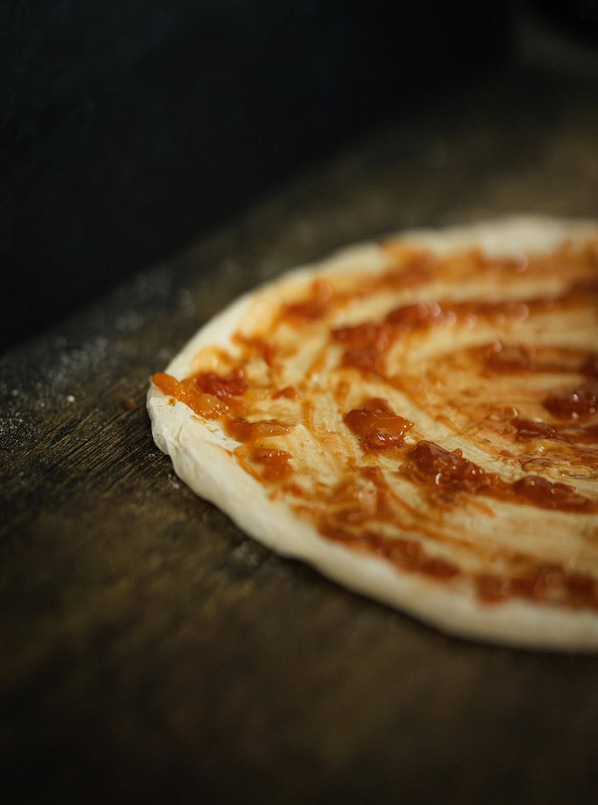 Fresh pizza dough spread with tomato base on a floured surface