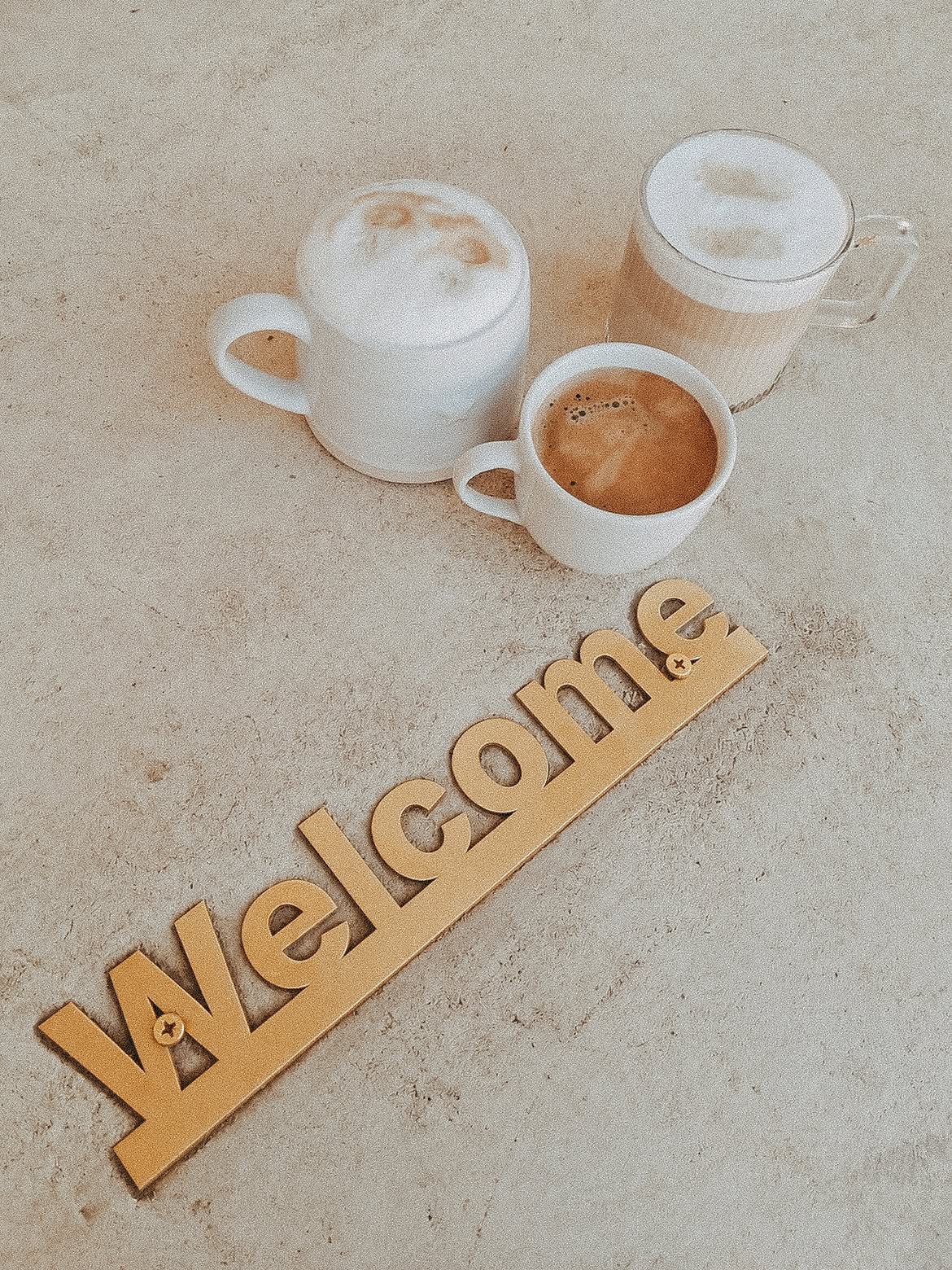 Three cappuccinos beside a gold Welcome sign on a stone table