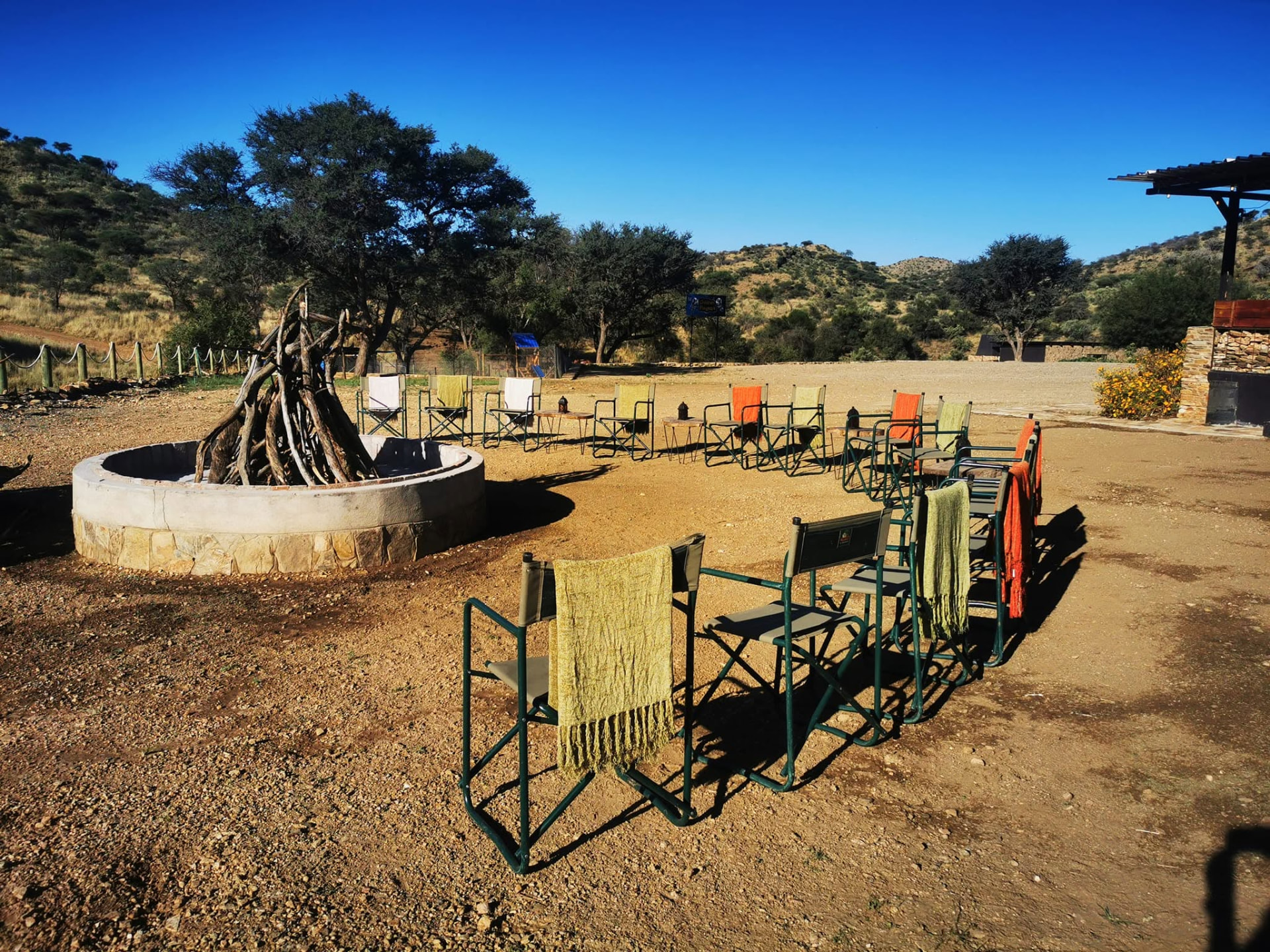 Directors' chairs with blankets arranged around a stone fire pit under a camel thorn tree