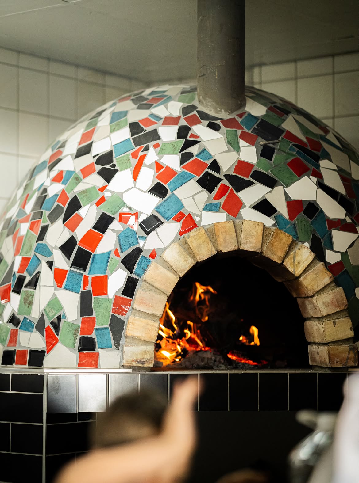 Mosaic-tiled wood-fired pizza oven with a fire burning inside