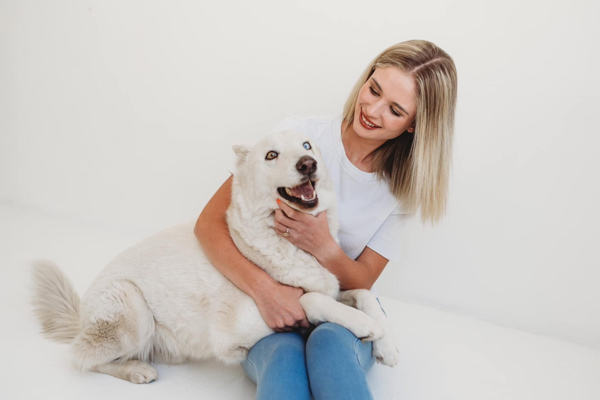 Owner sitting with a white husky against a plain backdrop