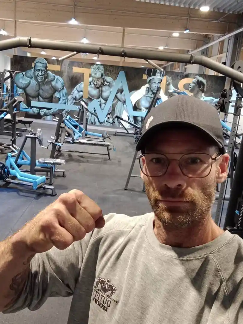 Rowan in the indoor gym surrounded by strength machines and a bodybuilding mural