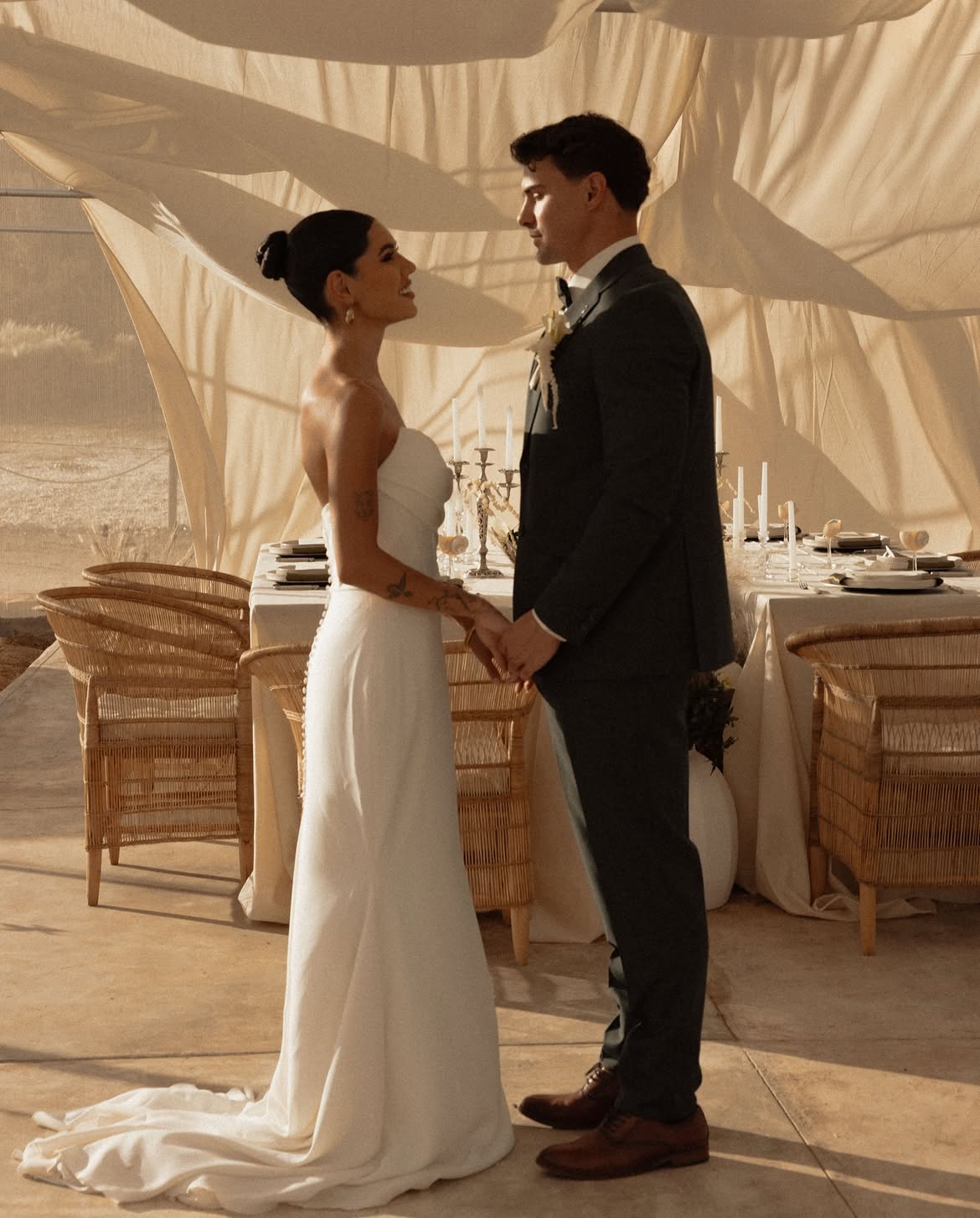 Bride and groom holding hands beside a candlelit table under draped linen