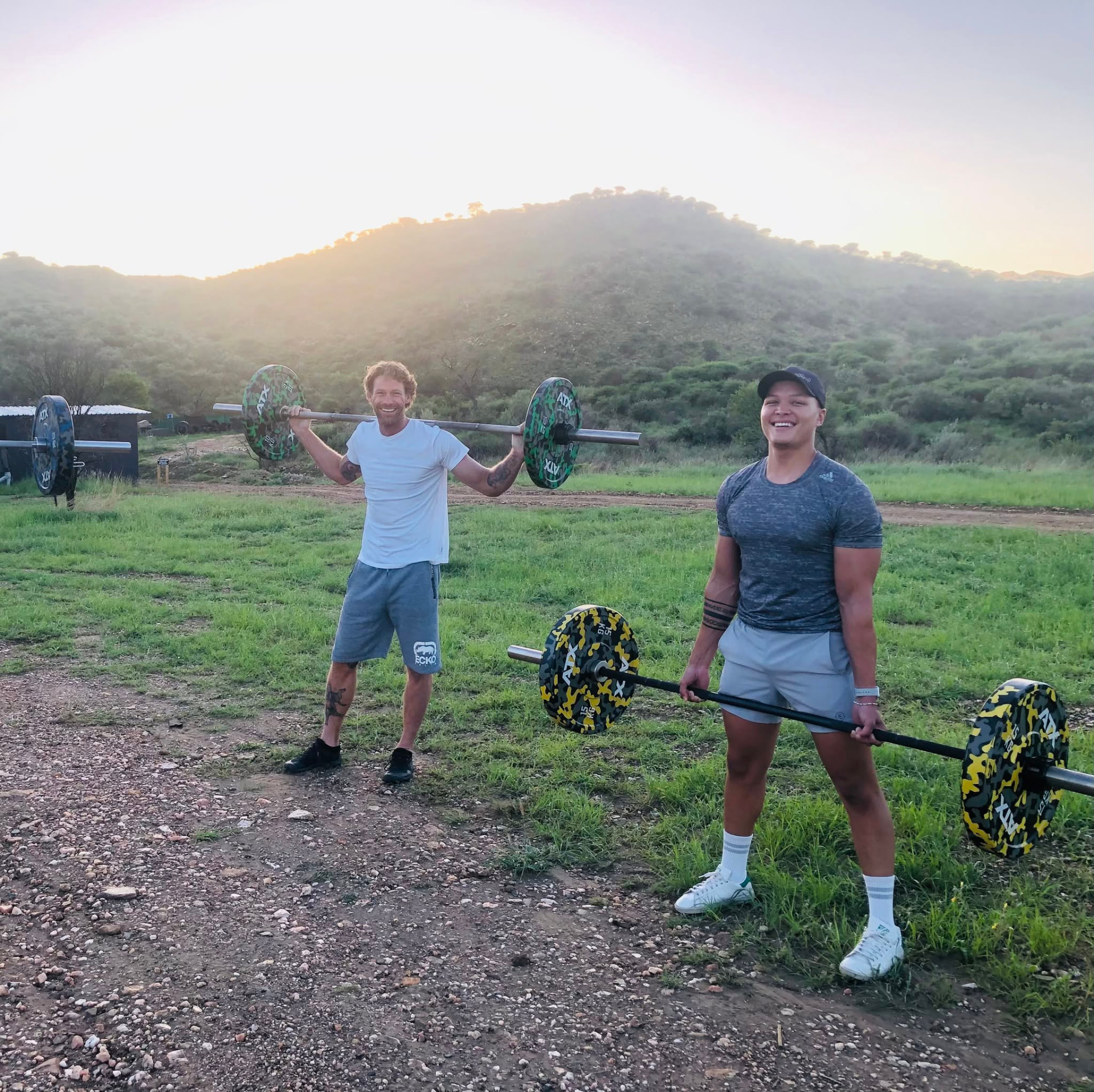 Athletes training with barbells outdoors at sunrise